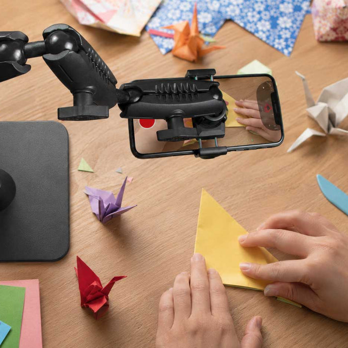 Yop down image of a content creator stand holding a phone while a pair of hands are creating some origami