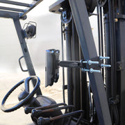 Close-up of a forklift cockpit featuring the 7.25 inch Metal Robust Forklift Front Guard Slim-Grip® Tablet Mount, securely holding a tablet next to the steering wheel and levers. A white brick wall is visible in the background.