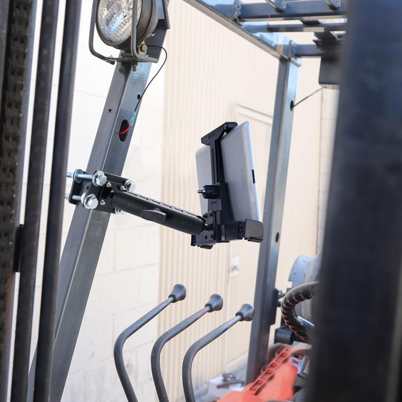 The LockVise™ Locking Forklift Front Guard Tablet Mount with 7.25 Shaft is securely installed inside a forklift cab near the controls, with an industrial building wall visible in the background.