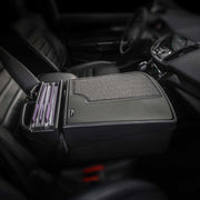 A car’s front seat interior showcases the Arkon Mounts AutoExec GripMaster Car Desk on the passenger seat, serving as a mobile workstation. This setup allows files or folders to be neatly arranged in an upright divider, topped with a gray, textured cover for organization and convenience.