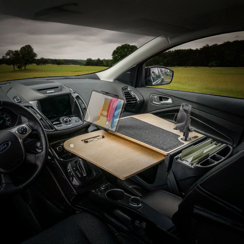 A car interior featuring the AutoExec GripMaster Car Desk with Mega Grip™ and Slim-Grip® Ultra Pro Drill-Base Mounts installed over the front passenger seat, organized to hold a tablet, papers, files, a phone holder, and writing tools—creating a true mobile workstation—with a green field visible outside the windows.