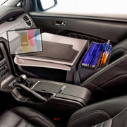 A car’s passenger seat holds an Arkon Mounts AutoExec GripMaster Car Desk with Slim-Grip® Ultra Pro Drill-Base Mount, featuring a document organizer, pens, and folders to transform the vehicle into a mobile workstation. The dashboard and gear shift appear in the foreground.