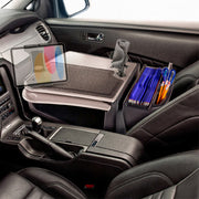 Inside a black vehicle, the AutoExec GripMaster Car Desk with Mega Grip™ and Slim-Grip® Ultra Pro Drill-Base Mounts transforms the front passenger seat into an efficient mobile workstation, complete with a tray table holding a tablet, smartphone, folder organizer filled with blue files, scissors, and pens.