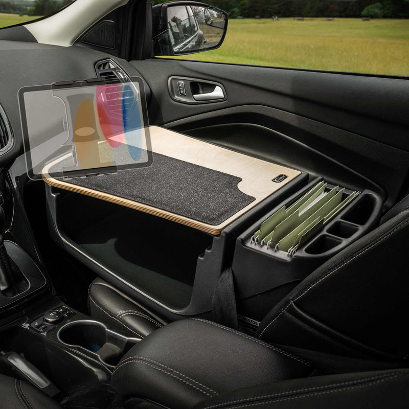 Transformed into a mobile office, the car’s front passenger seat area features the AutoExec GripMaster Efficiency Car Desk with Slim-Grip® Ultra Pro Multi-Angle Mount by Arkon Mounts—a wooden workspace equipped with a black mat and an organizer for hanging file folders. This dedicated car desk is ideal for productivity on the go, with grassy fields visible through the window in the background.