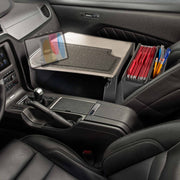 The front seat of a car features the GripMaster Efficiency Car Desk with Slim-Grip® Ultra Pro Drill-Base Mount by Arkon Mounts, equipped with a tablet holder, file organizer containing red folders, and pens—creating a mobile office workspace that installs securely with the convenient drill base mount.