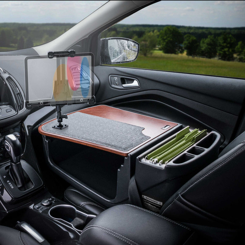 The AutoExec GripMaster Efficiency Car Desk, featuring a LockVise® Locking Tablet Holder and Multi-Angle Mount, is set up as a mobile workstation on the car’s passenger seat. Green file folders are organized within the desk’s compartments, with a scenic countryside view visible through the window.