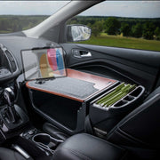 The Arkon Mounts AutoExec GripMaster Efficiency Car Desk with Slim-Grip® Ultra Pro Multi-Angle Mount transforms your car’s passenger seat into a functional mobile office, showcasing a sturdy desk setup with room for your laptop, organized files in the folder organizer, and an adjustable mount—all enhanced by the view of a green landscape through the window.