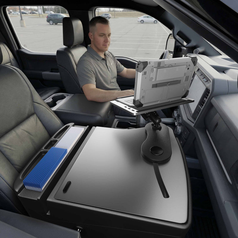 A man sits in a parked vehicle using a laptop mounted to the Arkon Mounts AutoExec Reach Front Seat Car Desk, with office supplies and folders neatly organized on the center console, creating an efficient car workspace for productivity on the go.