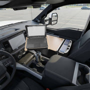 An AutoExec Reach Front Seat Car Desk by Arkon Mounts is attached to the passenger side of a vehicle interior, with a laptop placed on its surface. The car is parked in an empty parking lot, and a reusable travel mug sits in the desk’s cupholder, creating a convenient workspace for travelers.