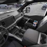 Interior of a pickup truck featuring the Portable Crate Workstation with Apron Organizer – Choose Your Mounting Setup in sleek black on the passenger seat, efficiently organizing a phone, notebook, and sunglasses. The parking lot and neighboring vehicles are visible through the windows, highlighting this workstation’s convenience for mounting devices and keeping essentials organized on the go.