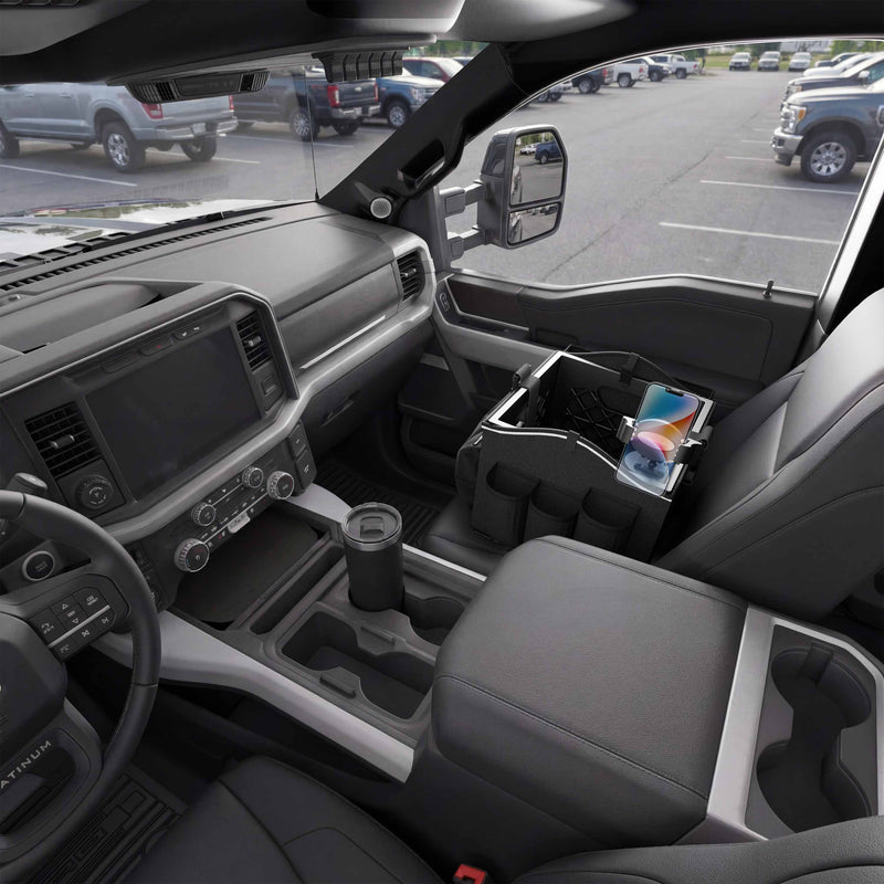 Interior of a pickup truck featuring the Portable Crate Workstation with Apron Organizer – Choose Your Mounting Setup in sleek black on the passenger seat, efficiently organizing a phone, notebook, and sunglasses. The parking lot and neighboring vehicles are visible through the windows, highlighting this workstation’s convenience for mounting devices and keeping essentials organized on the go.