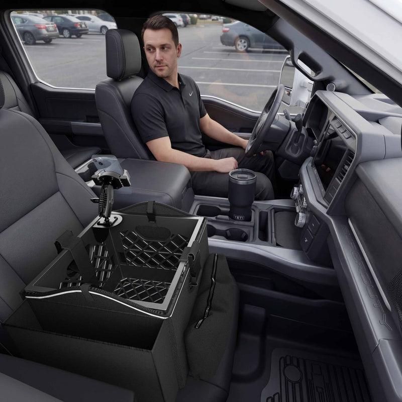 A man sits in the driver seat of a car, looking at the Portable Crate Workstation with Apron Organizer – Choose Your Mounting Setup, which features partitions and a mounted device on the passenger seat. The car’s interior is modern, and a parking lot is visible outside.