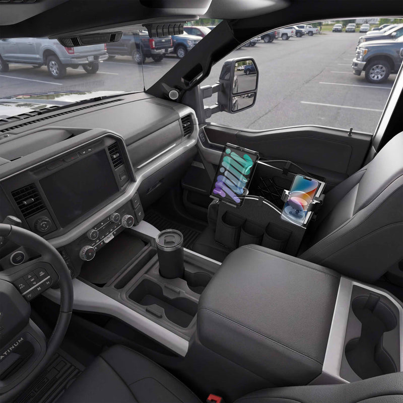 Inside a parked pickup truck, a Portable Crate Workstation with Apron Organizer—set up as a mobile workstation—securely holds both a tablet and a phone in the center console, while the windows reveal the parking lot and surrounding vehicles.