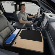 A man sits in the driver’s seat of a parked vehicle, using the GripMaster Efficiency Car Desk with Mega Grip™ Drill-Base Mount as a spacious mobile workstation, with organized files on the front passenger seat.