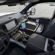 Inside the parked truck, the AutoExec GripMaster Efficiency Car Desk is set up between the front seats, featuring mounted Mega Grip™ and Slim-Grip® Ultra Pro Drill-Base Mounts that securely hold a tablet and smartphone. A travel mug rests in the cup holder, while the sturdy drill-base mounts keep devices stable and easily accessible for efficient work on the go.