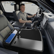 A man sits in the driver’s seat of a parked truck, with an AutoExec GripMaster Efficiency Car Desk set up in the front passenger area, along with files and office equipment. A Mega Grip™ and Slim-Grip® Ultra Pro Drill-Base Mount is also installed, keeping his tablet and other devices secure and accessible for efficient mobile work.