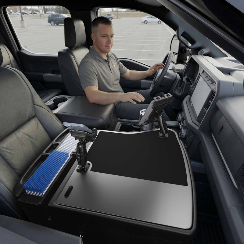 A man sits in the driver’s seat of a parked truck, with an AutoExec GripMaster Efficiency Car Desk set up in the front passenger area, along with files and office equipment. A Mega Grip™ and Slim-Grip® Ultra Pro Drill-Base Mount is also installed, keeping his tablet and other devices secure and accessible for efficient mobile work.