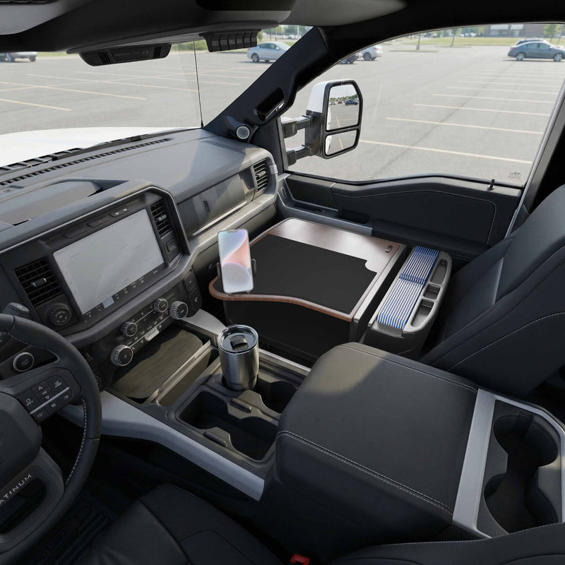 Inside the parked pickup truck, a GripMaster Efficiency Car Desk with Mega Grip™ Drill-Base Mount creates a spacious workspace tray over the passenger seat. A smartphone is held securely by the mounted Mega Grip™ drill-base, alongside a travel mug and a modern dashboard featuring a touchscreen. With the mostly empty parking lot outside, this setup makes for an ideal mobile workstation.