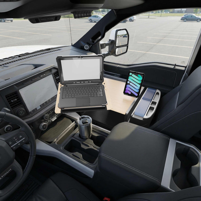 An AutoExec Reach Front Seat Car Desk with Slim-Grip® Ultra Pro Drill-Base Mount by Arkon Mounts is set up inside a parked vehicle, holding a laptop and tablet to create a comfortable mobile workspace, with a travel mug in the cup holder. The parking lot outside is mostly empty.
