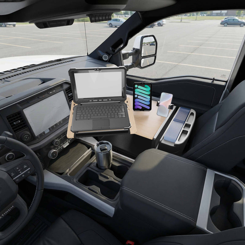 The AutoExec Reach Front Seat Car Desk with Slim-Grip® Ultra Pro and RoadVise® Ultra Pro Drill-Base Mount is set up inside a parked vehicle, holding a laptop, a tablet secured in the included holder, a mug, and various small items, with an empty parking lot visible through the driver’s side window.