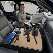 A man sits in a parked vehicle, working on his laptop mounted to the AutoExec Reach Front Seat Car Desk with Slim-Grip® Ultra Pro and RoadVise® Ultra Pro Drill-Base Mount, which covers the passenger seat and features convenient holders for devices and files, creating an efficient mobile workstation.