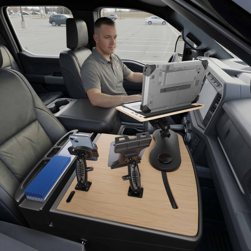A man sits in a parked vehicle, working on his laptop mounted to the AutoExec Reach Front Seat Car Desk with Slim-Grip® Ultra Pro and RoadVise® Ultra Pro Drill-Base Mount, which covers the passenger seat and features convenient holders for devices and files, creating an efficient mobile workstation.