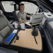 Using the AutoExec Reach Front Seat Car Desk with LockVise™ Locking Tablet Multi-Angle Mount, a man sits in the driver’s seat of his parked vehicle, working efficiently at a mounted laptop and secured tablet setup on the wooden desk that spans the passenger seat, creating a functional mobile workstation.