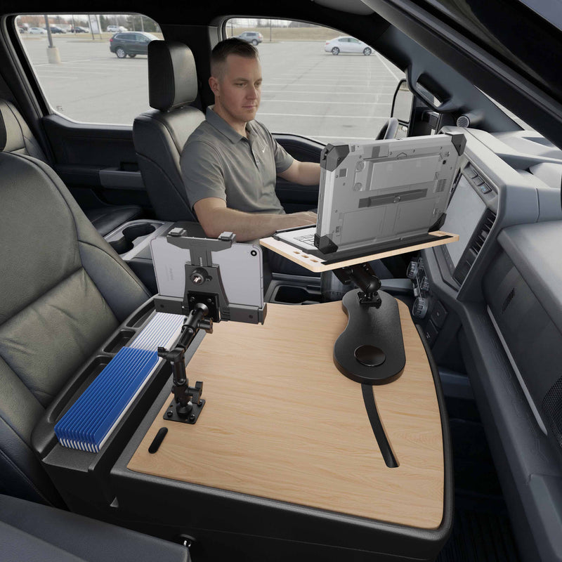 Using the AutoExec Reach Front Seat Car Desk with LockVise™ Locking Tablet Multi-Angle Mount, a man sits in the driver’s seat of his parked vehicle, working efficiently at a mounted laptop and secured tablet setup on the wooden desk that spans the passenger seat, creating a functional mobile workstation.