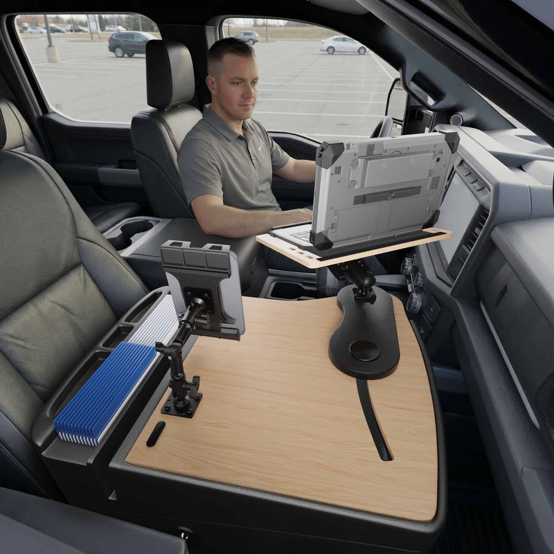 A man sits in a parked vehicle using the AutoExec Reach Front Seat Car Desk with Slim-Grip® Ultra Pro Multi-Angle Mount by Arkon Mounts, featuring a wooden car desk and multi-angle laptop and tablet holders attached to the passenger seat area.