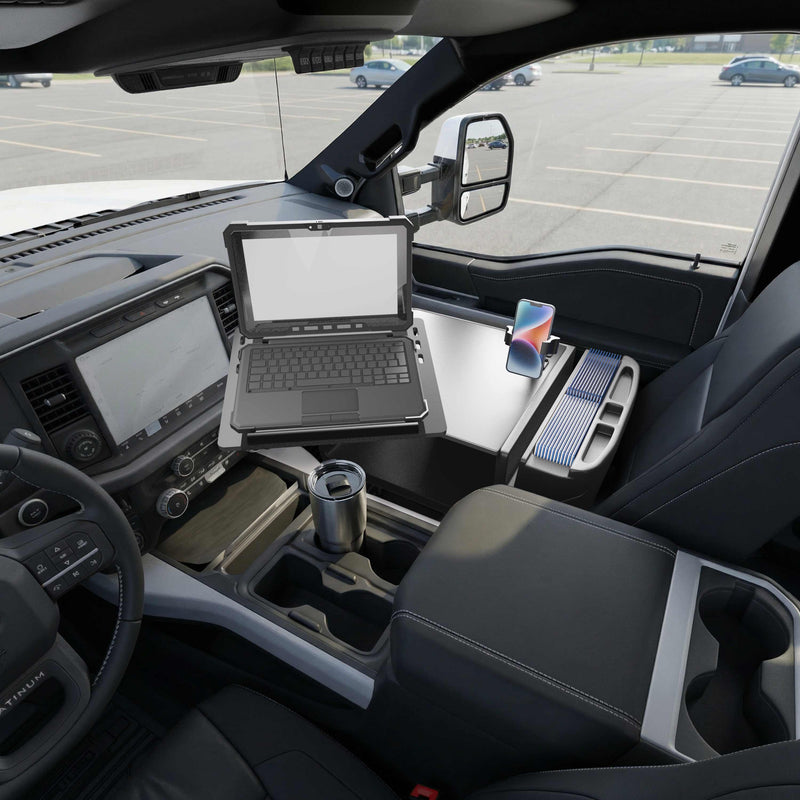An AutoExec Reach Front Seat Car Desk with RoadVise® Ultra Pro Drill-Base Mount supports a rugged laptop, smartphone, and travel mug, transforming the vehicle’s front seat into a fully equipped mobile workstation; the integrated phone holder securely cradles the device as empty parking spaces stretch out beyond the window.