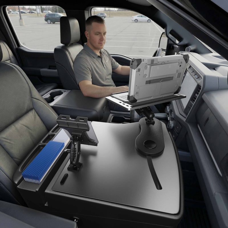 A man sits in the driver’s seat of a parked vehicle, working from a mobile office equipped with the AutoExec Reach Front Seat Car Desk featuring Arkon Mounts’ Slim-Grip® Ultra Pro Drill-Base Mount for his laptop and tablet. The setup provides a spacious surface area and organized storage compartments for efficient on-the-go productivity.