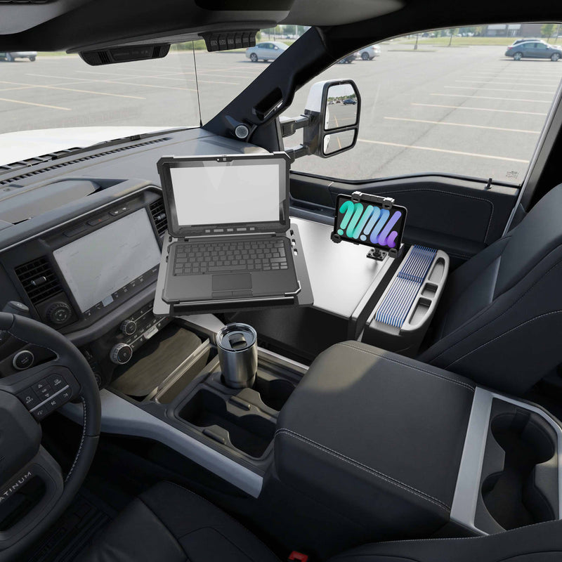 The AutoExec Reach Front Seat Car Desk with LockVise™ Locking Tablet Multi-Angle Mount holds a laptop and tablet securely inside a parked vehicle, creating a convenient mobile workstation. A cup rests in the holder, with the parking lot visible through the windows.
