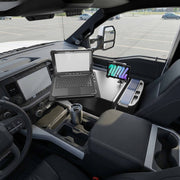 A truck interior is equipped with the AutoExec Reach Front Seat Car Desk, which includes a LockVise™ Locking Tablet Multi-Angle Mount to keep your device secure while you work. The setup features a mobile workstation with space for a laptop, travel mug, and storage organizer on the front passenger side. The vehicle is parked in an empty lot.