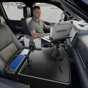 A man sits in the driver’s seat of a parked vehicle, working on his laptop using the AutoExec Reach Front Seat Car Desk with LockVise™ Locking Tablet Multi-Angle Mount, which also secures his tablet and keeps a notepad within reach, creating an efficient mobile workstation that doubles as his car desk.