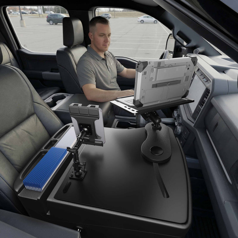 A man sits in the driver’s seat of a parked vehicle, working on his laptop mounted to the AutoExec Reach Front Seat Car Desk with Slim-Grip® Ultra Pro Multi-Angle Mount by Arkon Mounts, a versatile mobile workstation featuring an additional tablet holder, file organizer, and spacious work surface.