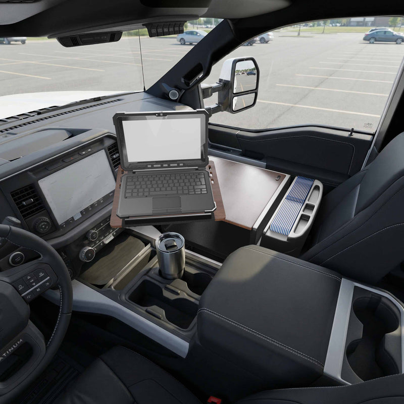 An Arkon Mounts AutoExec Reach Front Seat Car Desk holds an open rugged laptop, transforming the front passenger seat of a parked truck into a practical mobile workspace. The swivel workstation, truck dashboard, travel mug in the cup holder, and parking lot outside are all visible.