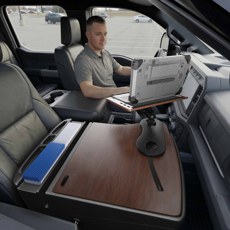 A man sits in the driver’s seat of a vehicle, using an Arkon Mounts AutoExec Reach Front Seat Car Desk with a wood finish and organized file folders nearby—creating an efficient car workspace.