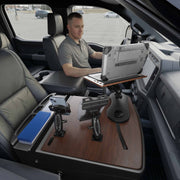 A man sits in the driver’s seat of a parked vehicle, working on a laptop mounted on the AutoExec Reach Front Seat Car Desk with Slim-Grip® Ultra Pro and RoadVise® Ultra Pro Drill-Base Mount, creating a modern, organized mobile workstation within the car interior.
