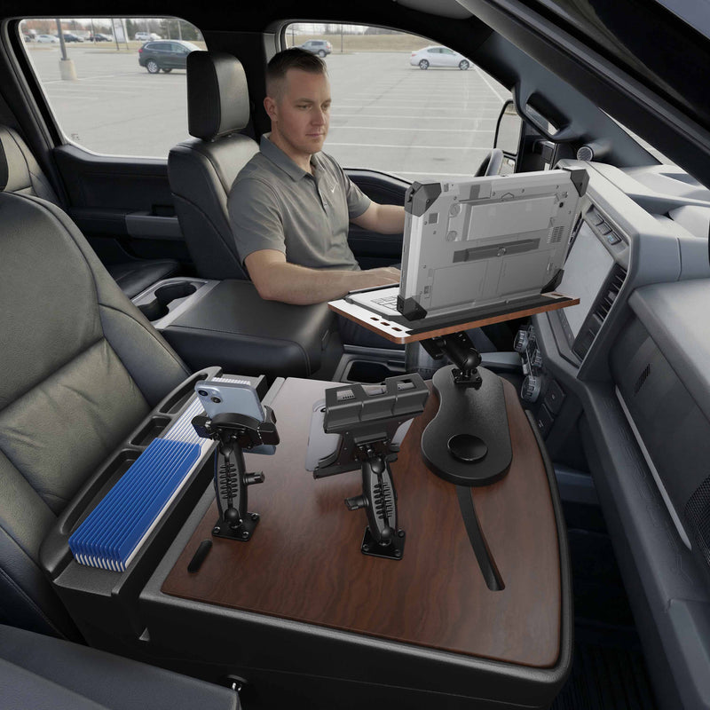 A man sits in the driver’s seat of a parked vehicle, working on a laptop mounted on the AutoExec Reach Front Seat Car Desk with Slim-Grip® Ultra Pro and RoadVise® Ultra Pro Drill-Base Mount, creating a modern, organized mobile workstation within the car interior.