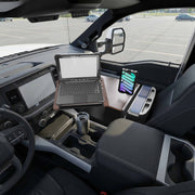 An AutoExec Reach Front Seat Car Desk by Arkon Mounts, featuring a Slim-Grip® Ultra Pro Multi-Angle Mount, is set up in the front seat of a truck parked in an empty lot, holding a laptop, smartphone, and travel mug to create an efficient mobile workstation.