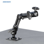 A black Camera Wall Mount with Multi-Angle Arm for Security Camcorders & Cameras is attached to a flat gray surface, features multiple joints and knobs for positioning, and displays the Arkon Mounts logo in the top left corner.
