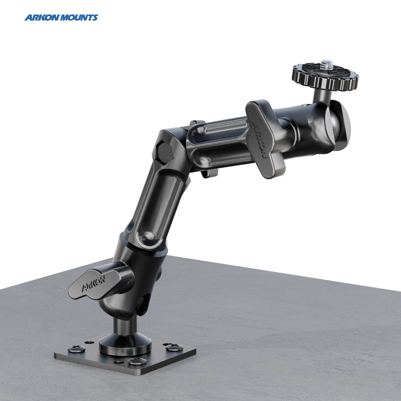 A black Camera Wall Mount with Multi-Angle Arm for Security Camcorders & Cameras is attached to a flat gray surface, features multiple joints and knobs for positioning, and displays the Arkon Mounts logo in the top left corner.