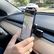 A hand holds a smartphone displaying a navigation map attached to an Arkon Mounts Magnetic Vent Phone Mount for Tesla Model 3 2017–2022 & Model Y 2020–2023 on a car dashboard.