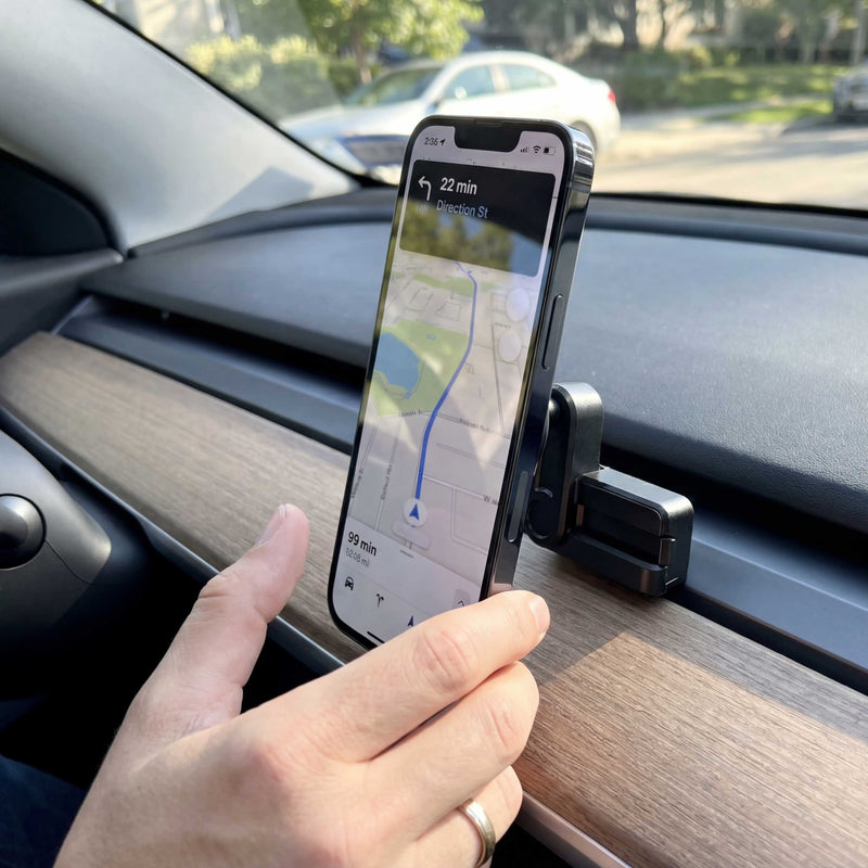 A hand holds a smartphone displaying a navigation map attached to an Arkon Mounts Magnetic Vent Phone Mount for Tesla Model 3 2017–2022 & Model Y 2020–2023 on a car dashboard.