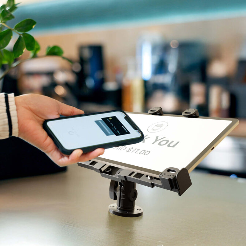 A hand holds a smartphone over a digital payment terminal to complete a contactless transaction. The terminal screen displays “Thank You” along with the paid amount of $11.00, while the LockVise™ POS Drill-Base Locking Tablet Mount keeps the checkout device securely in place for smooth processing.