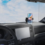 A modern vehicle’s interior features a smartphone securely mounted on the RoadVise® Ultra Pro Phone Holder 5” AMPS Drill-Base Mount, with the car’s steering wheel, expansive center display, and a clear sky visible through the windshield.
