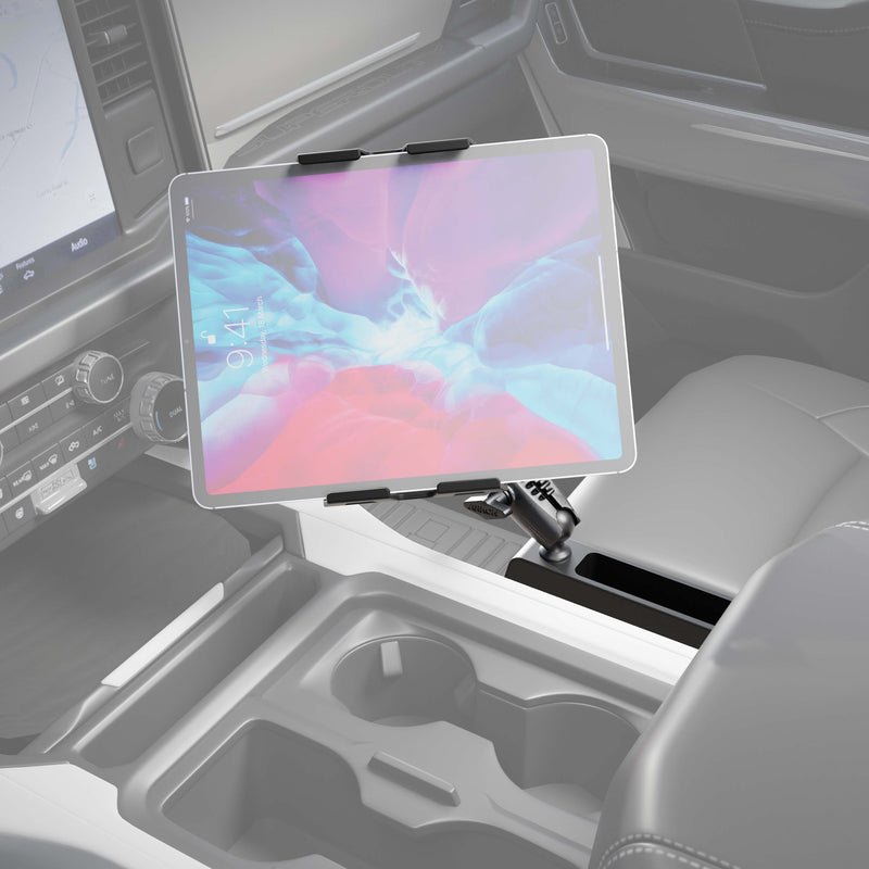 A Heavy-Duty Truck Console Wedge Slim-Grip® Ultra Pro Tablet Holder is mounted on a stand attached to a truck’s center console, positioned above the cupholders and next to the driver’s seat. The dashboard and controls are partially visible, making this tablet holder an ideal choice for convenient device access while on the road.