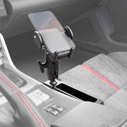 A smartphone sits in the Car Console Wedge Mega Grip™ Phone Mount Holder on the center console, beside the gear shift and cup holder. The interior features gray fabric seats accented with red stitching and trim.
