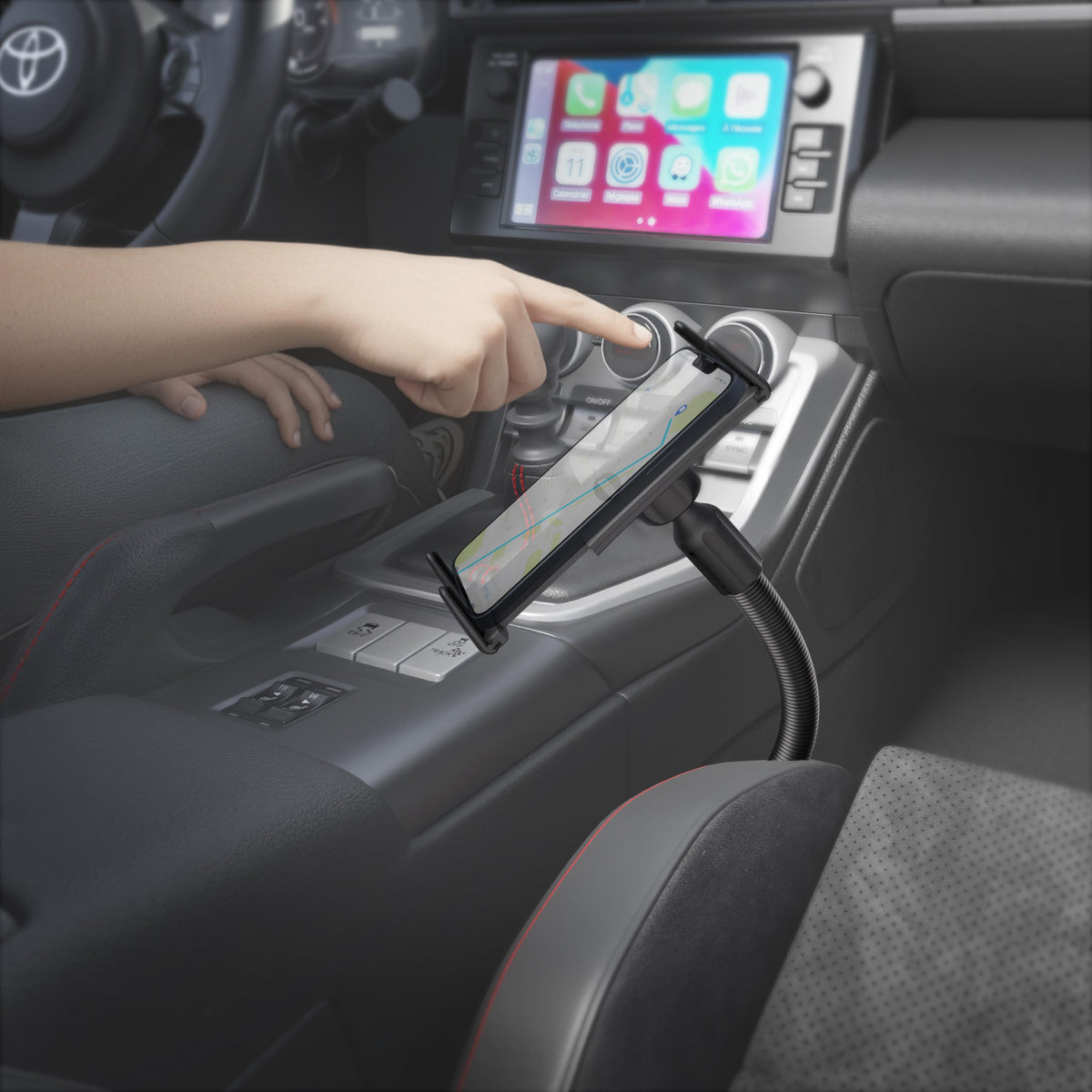 A person interacts with a smartphone secured in a Slim-Grip® Ultra 18″ Seat Rail or Floor Car Mount inside a car, with a navigation map shown on the phone’s screen and the car’s infotainment system visible in the background.