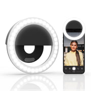 The Rechargeable Clip-On LED Ring Light is displayed solo and clipped to a smartphone, casting bright light on a woman’s face for ideal selfies or flawless makeup.